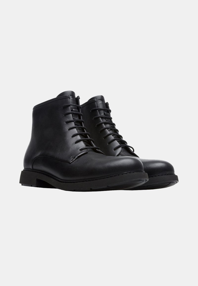 Botas de tobillo de cuero negro con una textura suave, punta redonda y cordones tradicionales. Suelas de goma resistentes con un diseño minimalista.
