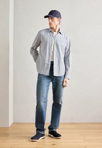 Meeste riietus, mis sisaldab sinise ja valgetriibulist särki, tumedaid teksaseid, tumesinist mütsi ning musti libisemisjalanõusid heleda tallaga.