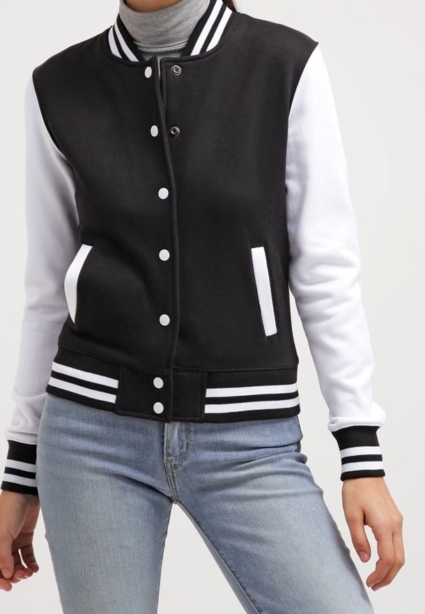 Veste universitaire noire et blanche avec col, poignets et ourlet rayés, portée par-dessus un col roulé gris et un jean bleu clair.