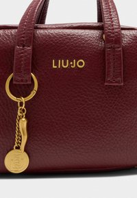Sac à main en cuir bordeaux avec finition texturée, quincaillerie dorée, logo embossé et accent d'un porte-clés décoratif.