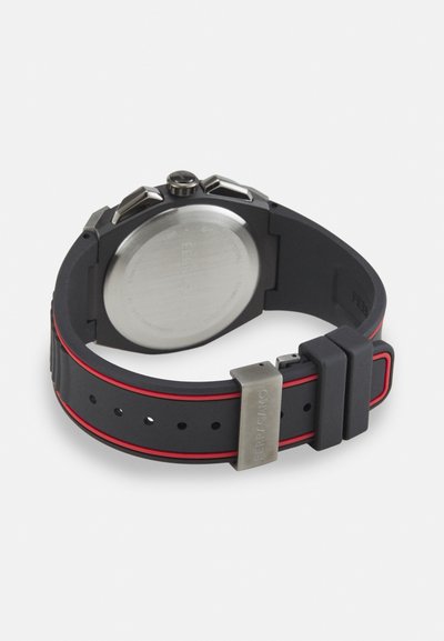 Black silicone watch strap with red accents, stainless steel buckle, round case with textured crown, and a smooth metallic back.