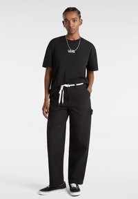 Sort bomulds T-shirt med hvid "VANS" logo, parret med løse sorte bukser med et hvidt bælte, iført sorte sneakers.
