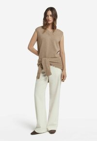 Beige stickad ärmlös topp med V-ringning, tillsammans med vita ribbade vida byxor. Toppen är knuten i midjan med ett matchande tyg.