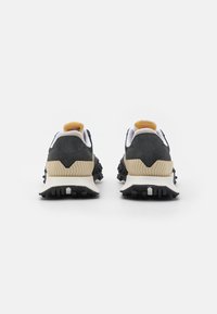 Ett par svarta och beige sneakers med texturerade sulor visade framifrån på en enkel vit bakgrund.