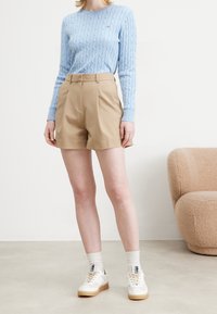 Jasnoniebieski sweter w splot warkoczowy, beżowe plisowane szorty, białe trampki z kremowymi podeszwami i białe skarpetki. Prosty, nowoczesny design i miękka tekstura.