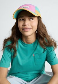 Mėlynos spalvos trumpomis rankovėmis marškinėliai su kišene ir spalvingas kepuraitė, kuri turi rožinius, žalius ir geltonus intarpus. Sklandus audinys su laisvu stiliumi.