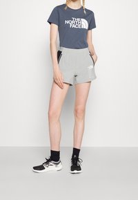 Szorty w kolorze szarym z czarnymi akcentami i białym logo, do tego ciemnoszara koszulka z białym nadrukiem. Noszone z czarnymi butami sportowymi i skarpetami.