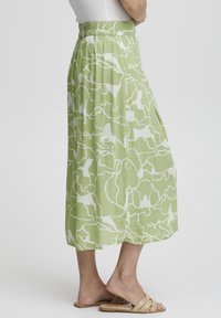Roheline midi-seelik valge abstraktse mustriga, elastne vöökoht, voolav kangas ja küljetaskud. Kantud beežide libisevate sandaalidega.