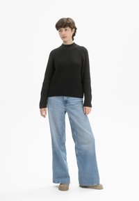 Schwarzer, gerippter Pullover mit hohem Kragen und Raglanärmeln, kombiniert mit hellblauen, weit geschnittenen Jeans und braunen Slippern.