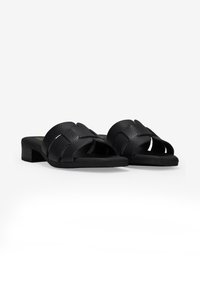 Sandalias deslizantes de cuero negro con un diseño de tirante texturizado, punta abierta y un bajo tacón cuadrado. La suela es plana y lisa.
