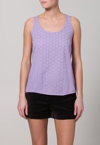 Lilac sleeveless tank top with a patterned eyelet design on the front, made from lightweight fabric. Paired with black shorts.