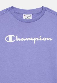 Μωβ κοντομάνικη μπλούζα με στρογγυλή λαιμόκοψη και λευκό λογότυπο "Champion" στο στήθος, μέγεθος μικρό για ηλικίες 7-8 ετών, κατασκευασμένη από μαλακό βαμβακερό ύφασμα.