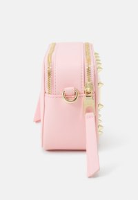 Różowa torba z eko skóry z złotymi suwakami i kolcami wzdłuż jednej strony. Pasek do noszenia i metaliczne elementy podkreślają design. Kompaktowy, prostokątny kształt.