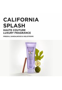 Lilla tube med Kérastase hårprodukt med hvite og fargerike detaljer, ledsaget av en kanelstang, bergamot og grønne blader.