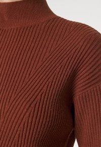 Rippstrick-Turtleneck-Pullover in dunklem Rostton, mit diagonalen Rippmuster und einem weichen, strukturierten Stoff.