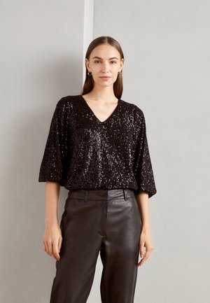 Schwarzes Paillettentop mit V-Ausschnitt, kurzen Ärmeln und oversized Schnitt, kombiniert mit schwarzen Lederhosen. Glatte Textur und auffälliger Glanz.
