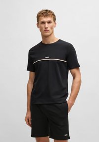 Schwarzes Baumwoll-T-Shirt mit Rundhalsausschnitt und kurzen Ärmeln, mit einem weißen "BOSS"-Logo und einem horizontalen Streifenakzent in Beige und Weiß.