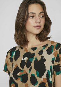 Top in stampa leopardata beige, con macchie astratte nere, verdi e marroni. Tessuto liscio, scollatura rotonda e maniche corte.