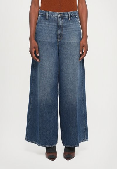 Jeans en denim bleu foncé à jambe large avec une taille haute, présentant un design classique à cinq poches et une texture décolorée vers l'ourlet.