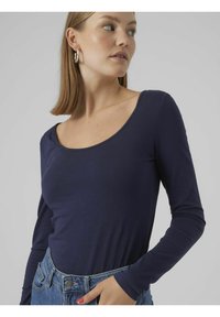 Marineblaues Langarmoberteil mit rundem Halsausschnitt, aus glattem Stoff, kombiniert mit hoch taillierten Jeans aus Denim.