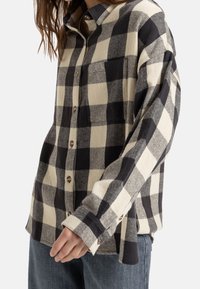 ternet flannel skjorte i sort og creme, med knaplukning fortil, lange ærmer og en brystlomme. Blød tekstur og afslappet pasform.