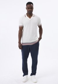 Polo blanco de manga corta con cuello y dobladillo a rayas en azul marino, rojo y blanco, combinado con pantalones azul marino y zapatillas blancas.