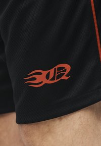 Μαύροι αθλητικοί σορτς από δίχτυ με κόκκινο φλεγόμενο λογότυπο μπάσκετ στο μηρό και πορτοκαλί ρίγα κατά μήκος της πλαϊνής ραφής.