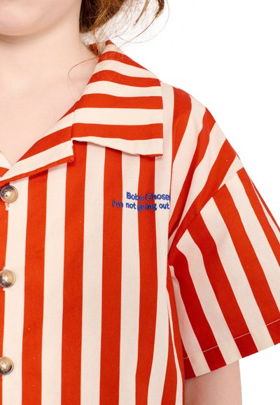 Chemise rayée rouge et blanche à rayures verticales, manches courtes, boutons argentés et texte bleu « Bobo Choses I'm not going out » sur la poitrine.