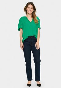 Grön, kortärmad blus med V-ringning, bärs med mörkblå, raka jeans och svarta ballerina. Slätt tyg med avslappnad passform.
