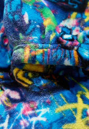 Tessuto in pile morbido con motivi astratti nei colori blu, giallo, verde e rosa brillanti in primo piano, che mostrano texture e colori vivaci.