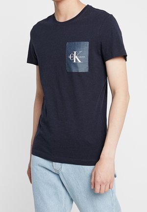 Marineblauw katoenen t-shirt met een ronde halslijn, voorzien van een dennenzak met een wit logo. Eenvoudig ontwerp, korte mouwen en een ontspannen pasvorm.