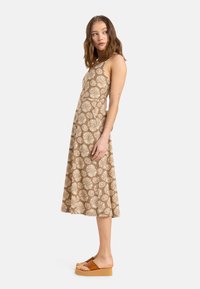 Brun blommig klänning med spaghettiband, knäl�ång fåll och vita prydnadsmargaretor. Bärs med beige plattformssandaler.