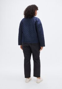 Σακάκι από ναυτικό μπλε καπιτονέ με υφή, άνετη εφαρμογή και πέφτοντες ώμους, συνδυασμένο με σκούρο παντελόνι και ανοιχτά αθλητικά παπούτσια.