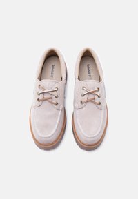 Παπούτσια από σουέτ σε ανοιχτό μπεζ χρώμα με κορδόνια, κεντήματα σε κρεμ απόχρωση και καφέ ελαστική σόλα. Διπλές τρύπες για κορδόνια με χρυσές μεταλλικές λεπτομέρειες.