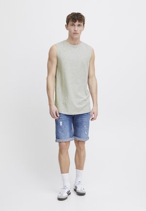 Lys grå ermeløs skjorte, blå denimshorts med rullekanter og slitte detaljer, hvite sokker og svart-hvite sneakers.