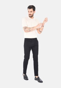 Polo shirt a coste di un beige chiaro, con maniche corte, abbinato a pantaloni neri slim-fit e mocassini neri, esposto su uno sfondo semplice.