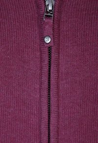 Kaštanový svetr na zip s žebrovanou texturou. Má kovový zip a stříbrný taháček. Hladká látka s přiléhavým střihem.