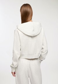 Felpa grigia chiara, tagliata, con cappuccio, maniche lunghe e orlo a costine, realizzata in un tessuto morbido e testurizzato, abbinata a pantaloni jogger coordinati.