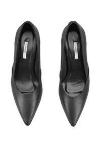 Une paire de chaussures à talons hauts en cuir noir, à bout pointu, avec l'étiquette "DESA" à l'intérieur, vue de dessus sur un fond blanc.