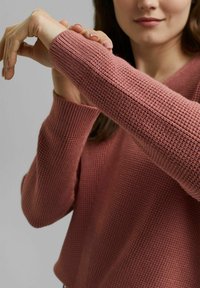 Pull-over en laine couleur rose poussiéreux, présentant un motif de tricot texturé et des manches ajustées. Le tissu a une texture douce et côtelée avec une coupe décontractée.