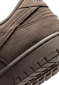 Gros plan sur le talon d'une basket en daim marron montrant la tige texturée, les détails cousus, le col rembourré et la semelle extérieure en caoutchouc à motifs.