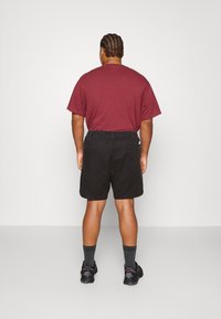 Marmoreret T-shirt og sorte shorts med elastisk talje, med lommer. Båret med grå sokker og sorte sneakers. Ensfarvet baggrund.