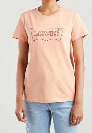 Personne portant un t-shirt Levi's rose clair et un jean bleu clair, debout avec les bras détendus le long du corps.