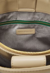 Interno di una borsa in pelle beige con una morbida fodera in tessuto grigio, dotata di una zip verde e di un'etichetta in pelle beige con la scritta "TOMMY HILFIGER" impressa.