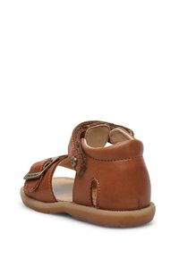 Brązowe skórzane sandały o teksturowanym wykończeniu. Posiadają regulowany pasek, okrągły czubek, wycięcia po bokach oraz gumową podeszwę dla lepszego chwytu.