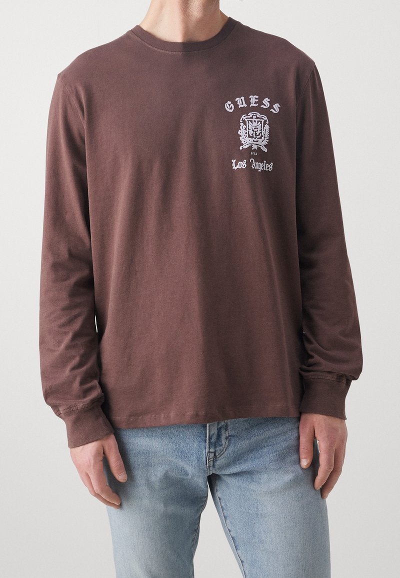 T-shirt a maniche lunghe marrone in cotone, con una stampa grafica sul lato sinistro del petto con "Guess" e "Los Angeles" in bianco.