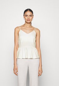 Lys gul peplum topp med justerbare spaghettistropper og V-hals. Laget av glat stoff med en avslappet silhuett. Kombinert med lyse bukser.