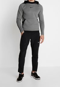 Sudadera gris de Nike con acentos negros, que presenta un bolsillo tipo canguro y un diseño ajustado. Combinada con pantalones negros y zapatillas deportivas negras.
