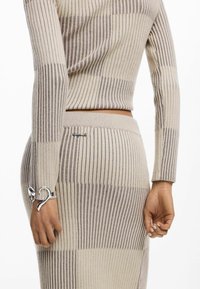 Conjunto de dos piezas de punto con textura acanalada en rayas beige y marrón claro. Los detalles incluyen un adorno plateado decorativo en la manga.