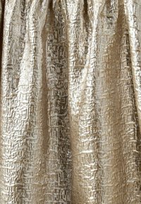 Skinande gyllene tyg med en texturerad mönster, med upphöjda geometriska mönster som skapar visuell djup och dimension.